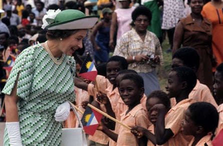 Queen Elizabeth II in Antigua in 1977: she is greeting a group of young schoolchildren. She wears a green hat and green patterned dress plus white gloves and holds a white handbag.