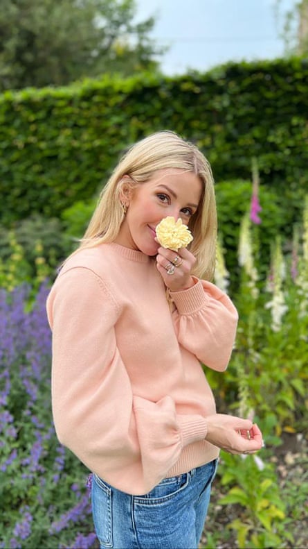 Ellie Goulding stands in a garden and holds a rose in front of her face