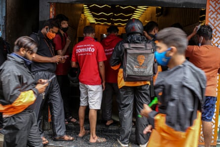 Delivery riders for Zomato and Swiggy, operated by Bundl Technologies, wait to collect orders outside a restaurant in Mumbai, India.