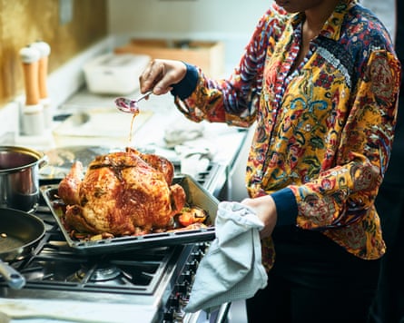 A woman holding a spoon and pouring oil over a roast turkey