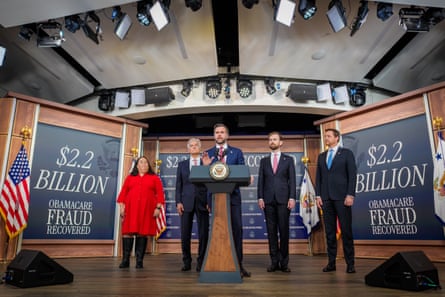 A man speaking at a lectern in front of four other people with posters saying ‘$22 billion Obamacare fraud uncovered’