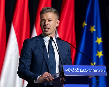 Magyar stands at a lectern, with flags in the background