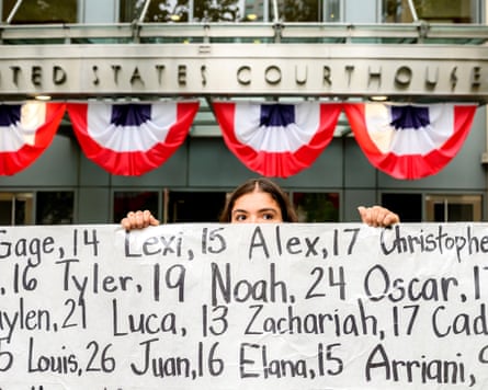 Person peers over top of banner with names and ages written on it