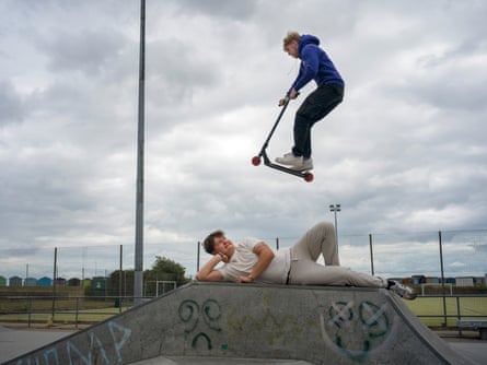A teenage boy flies through the air after launching himself off a ramp on a scooter while another boy lies underneath him