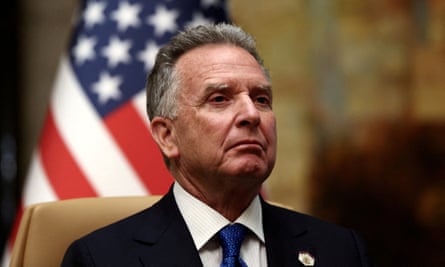 Steve Witkoff, a white man with short greying hair, sitting in front of an American flag wearing a dark suit and blue tie