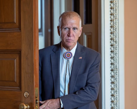 An older man in a western tie and a suit walks exits a room