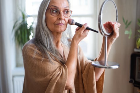 Senior woman looking at mirror and applying make up at home
