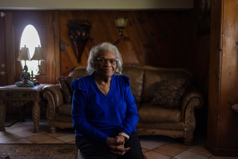A woman wearing a blue top sits insider her home with wood panel walls
