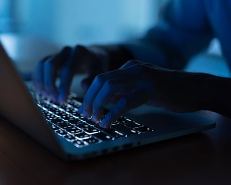 Close-up of hands typing on a backlit laptop keyboard in a dark room