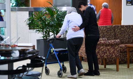 woman in an aged care home walking with walking frame with her carer