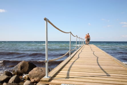 A man and a woman walking on a wooden jetty jutting into the sea on a warm and sunny summer day