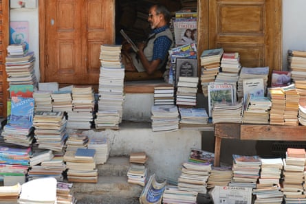 A bookseller sitting in a doorway with books arranged on the pavement