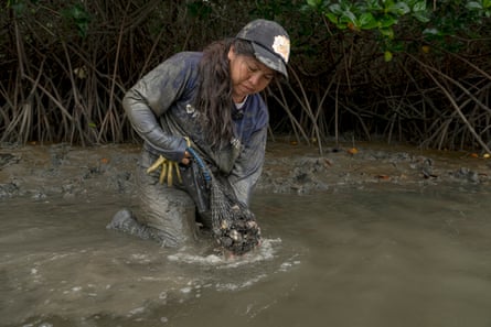 A woman stands knee-deep in water holding a bag of shellfish