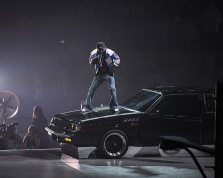 Kendrick Lamar standing on a car bonnet singing