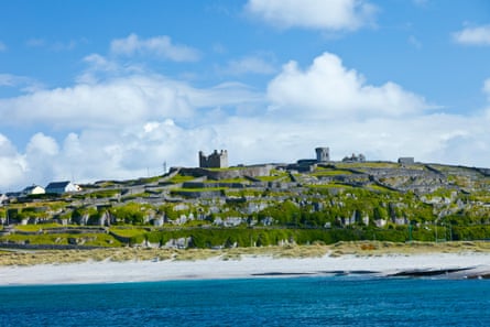 Ruins, stone walls and a couple of modern houses on an island, seen from the sea