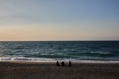 Women sit in the sand looking at the ocean