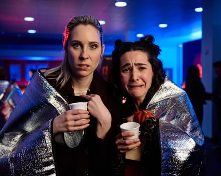 Two women in silver trauma blankets with paper cups in a cinema