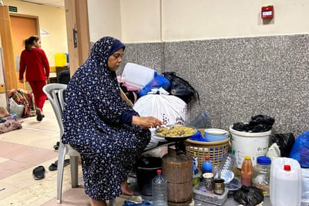 A refugee cooks prepares a meal in a hospital corridor on a gas stove 