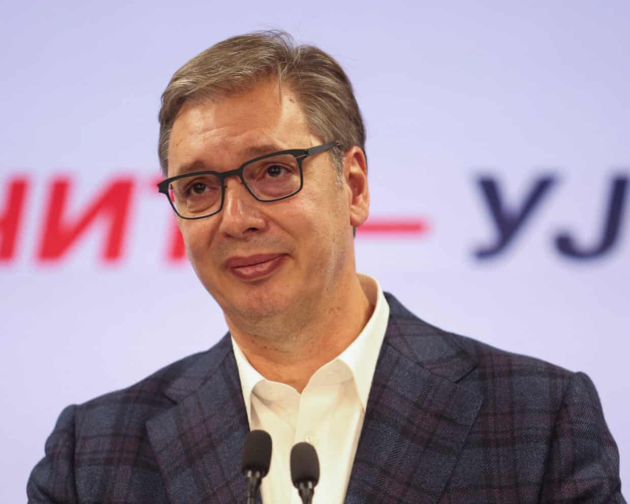 Wearing a checked jacket, cream shirt and glasses, Aleksandar Vučić looks sad as he concedes defeat in the Serbian election