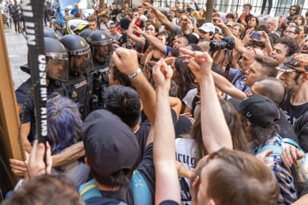 Protesters shout and raise their arms as they face riot police