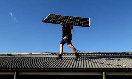A worker carries a solar panel on to the roof of a home in Sydney, Australia