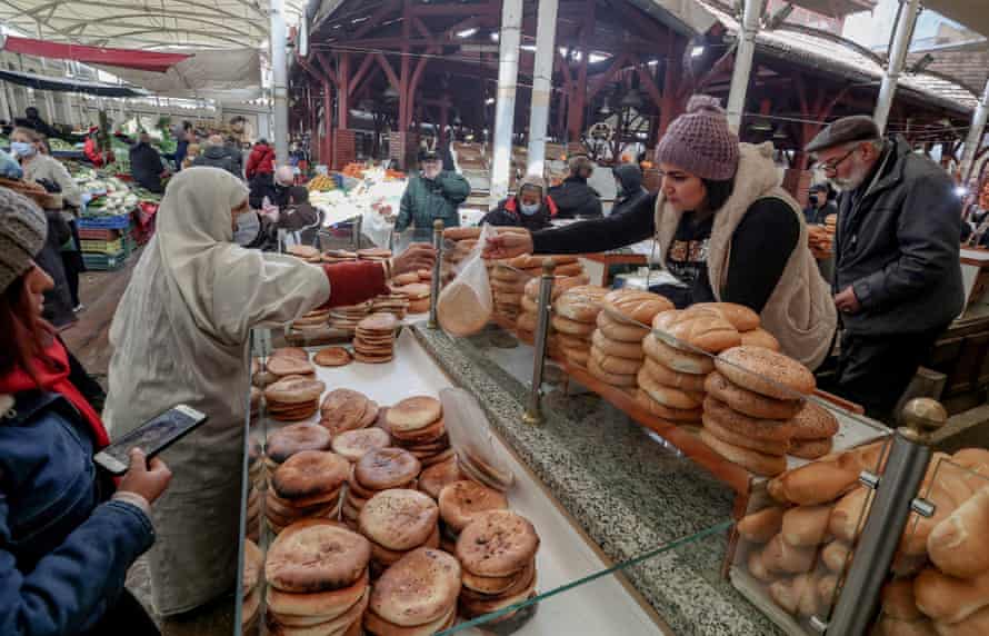 A veiled woman buys bread at a market stall