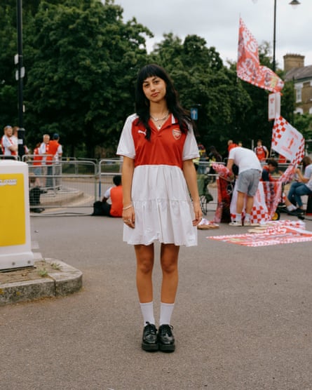 A young woman in a white skirt, red and white Arsenal shirt, white socks and black shoes