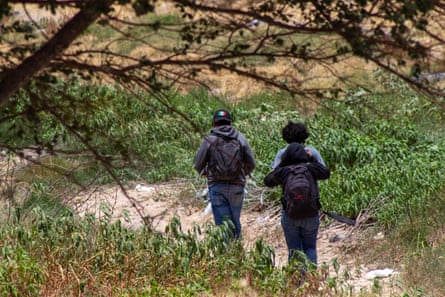 Three people walk through brush and dirt with backpacks on