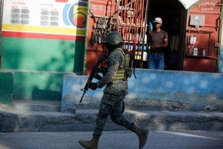 A soldier in fatigues with a gun runs past a building