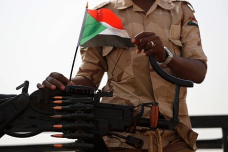 A soldier loads a rifle that carries a Sudan flag