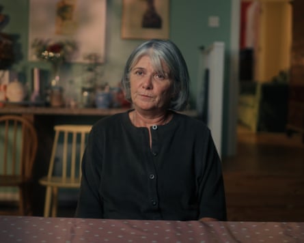 Robert McCartney's sister Catherine, wearing a black button-up top, sits at a table facing the camera in in Murder in Belfast: Sisters Seeking Justice