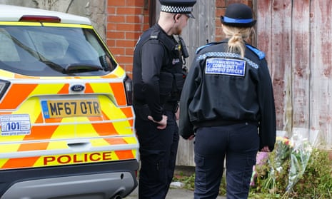 Police officers look at flowers left outside a property in Radcliffe.