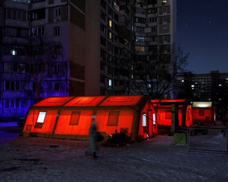 Red tents illuminated by light inside, next to high-rise blocks of flats.