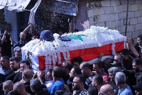 Mourners carry a coffin covered in flowers and a press helmet.