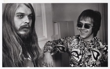 Black and white photo of Elton John, wearing glasses, smiling at a long-haired Leon Russell.