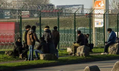 Migrants gather near a barbed wire fence at a truck parking lot in Calais