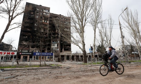 A man rides a bicycle near a destroyed residential building in Mariupol