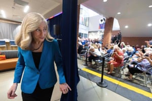 Well-groomed woman walking on stage with audience in chairs