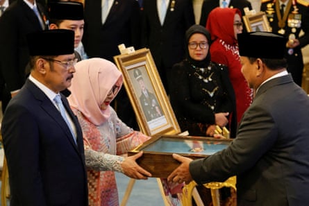 Subianto hands a glass-fronted wooden display case to Rukmana, who stands next to a portrait of a man in military uniform