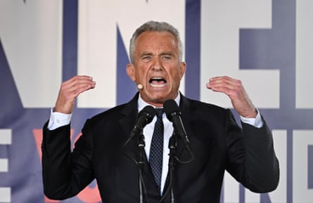 A man wearing a black suit speaks into a microphone with his hands in the air