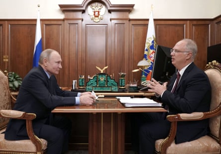 Putin and Dmitriev sit opposite one another at a small table. Dmitriev has pieces of paper spread out in front of him