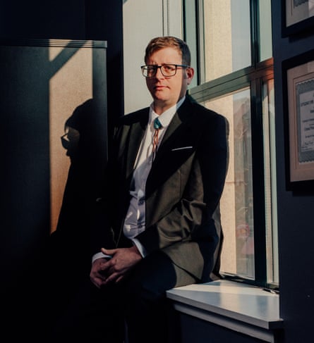 Eric Bisby sitting in his office, wearing a dark suit, white blouse and patterned tie, looking at the camera