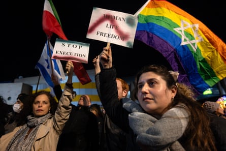 Women in the city of Holon, Israel, hold up signs reading ‘woman life freedom’ and stop execution and a rainbow flag