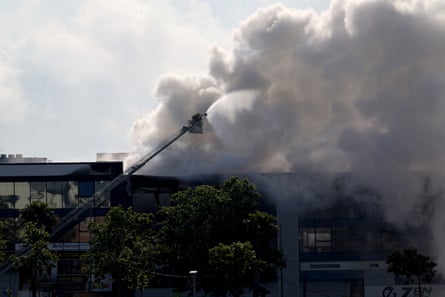 A firefighter in a cherrypicker sprays a hose on smoke billowing from a warehouse