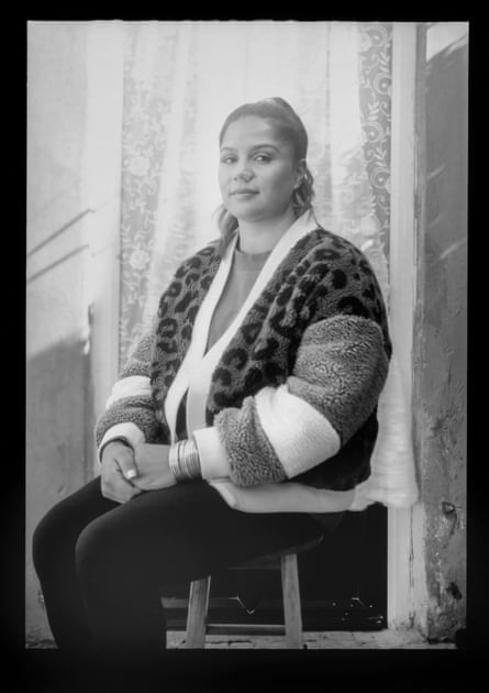 A woman sitting on a chair in front of a curtain.