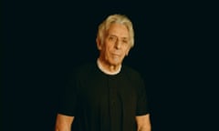 John Cale in a black T-shirt wearing a string of pearls.