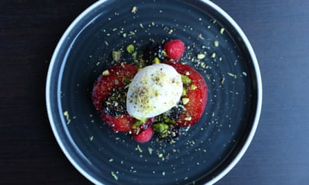 Purple roasted plums with white vanilla ice cream and green sprinkles of crushed pistachios on a dark blue round plate.