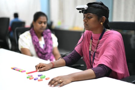 A woman wearing a camera on her head sits at a table with small coloured blocks in front of her. Another woman sits next to her