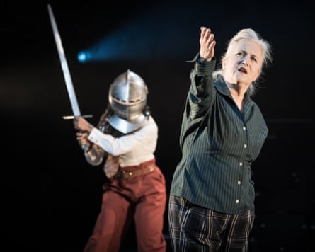 A woman in a knight’s helmet raises a sword behind an older woman in front of her who is raising her arm.