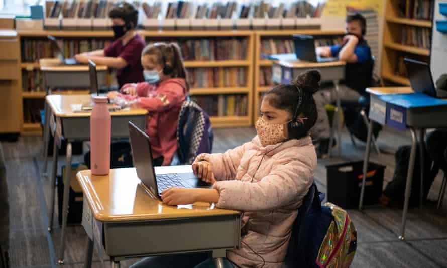 students in a classroom, seated behind desks, working on their own laptops